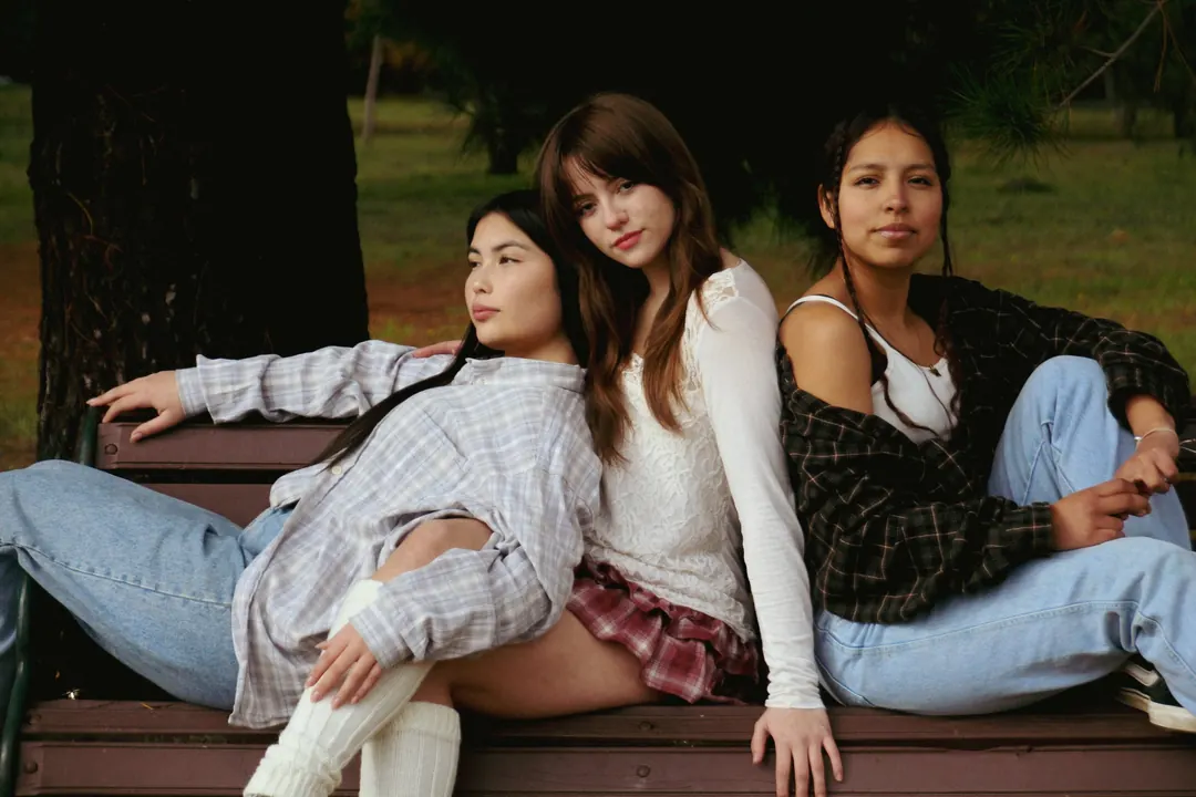 Tres jóvenes sentadas en una banca bajo los árboles