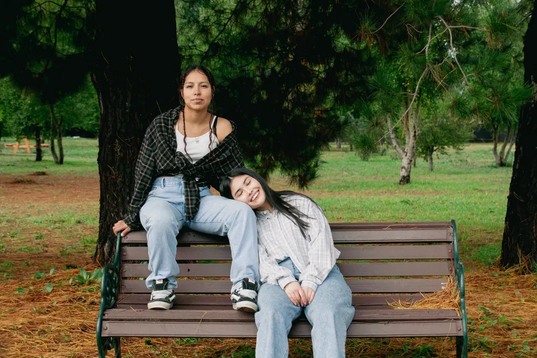 Dos jóvenes en una banca bajo un pino
